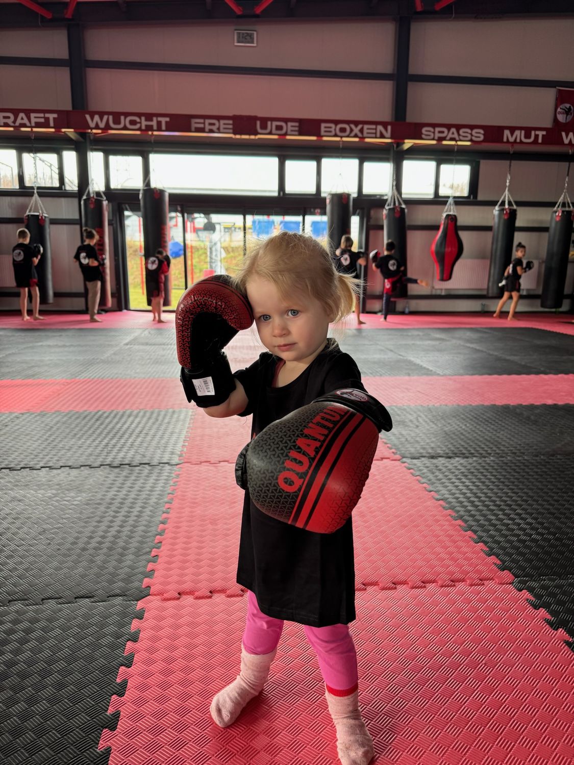 Kleines Mädchen mit Boxhandschuhen auf der Matte